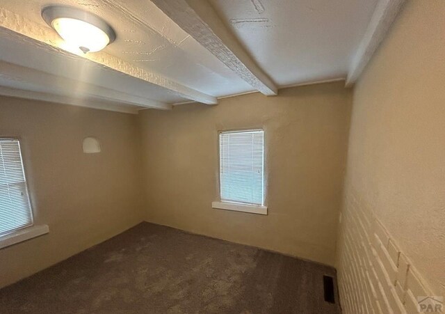 carpeted empty room featuring a wealth of natural light, visible vents, and beam ceiling