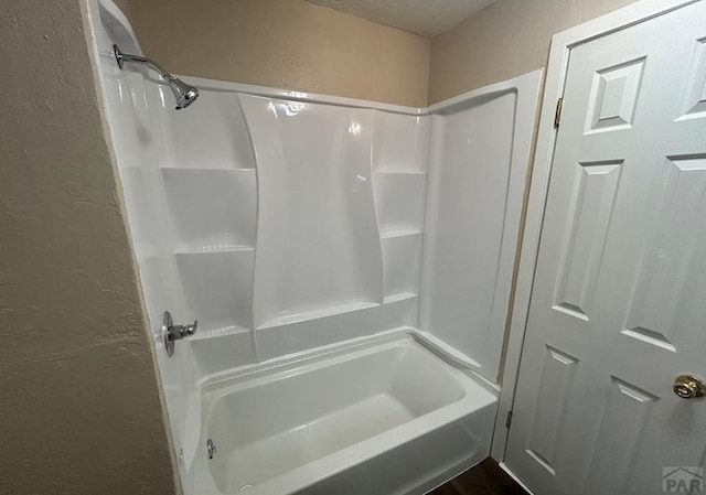 bathroom with shower / bathing tub combination and a textured wall