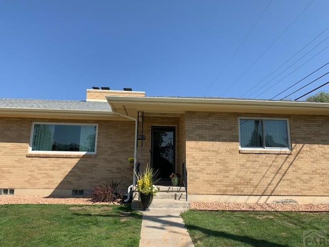 doorway to property featuring brick siding and a lawn