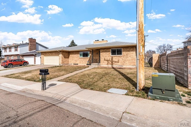 view of front facade featuring driveway, fence, a front yard, an attached garage, and brick siding