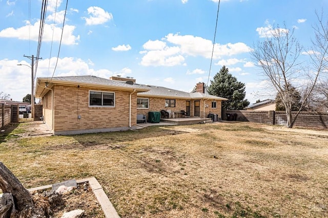 back of property with a lawn, a deck, a fenced backyard, brick siding, and a chimney