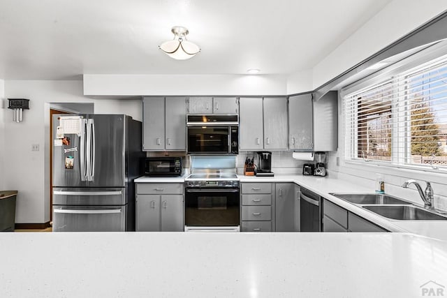 kitchen with tasteful backsplash, light countertops, gray cabinets, appliances with stainless steel finishes, and a sink