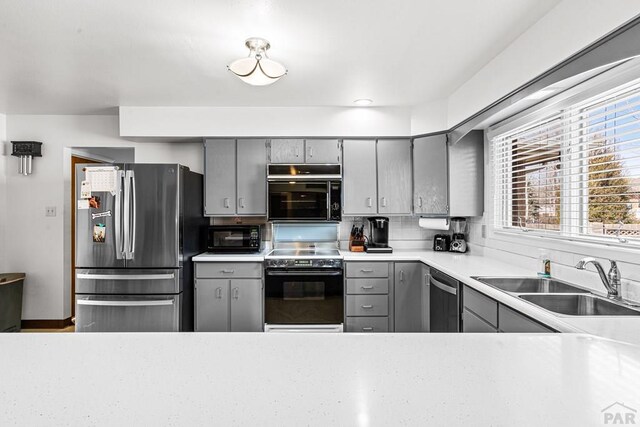 kitchen with gray cabinets, a sink, stainless steel appliances, light countertops, and decorative backsplash