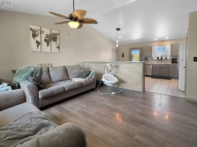 living area with light wood-style flooring, a ceiling fan, and vaulted ceiling
