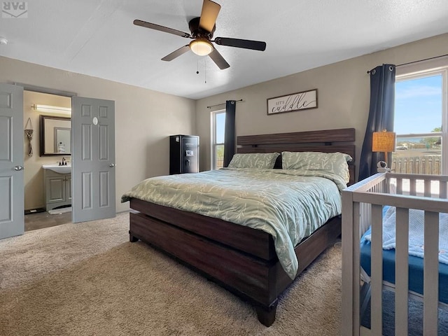 carpeted bedroom with ensuite bath, a sink, and a ceiling fan