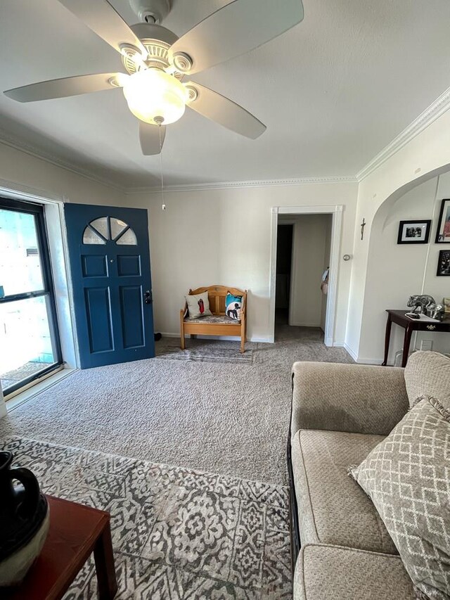 carpeted living area with arched walkways, ceiling fan, baseboards, and crown molding