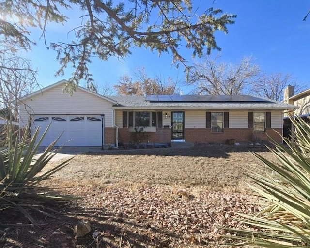 single story home featuring brick siding, solar panels, covered porch, an attached garage, and driveway