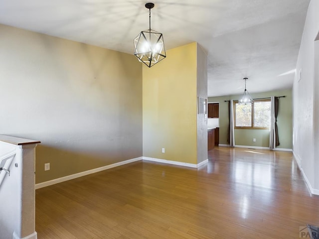 unfurnished dining area featuring wood finished floors, baseboards, and an inviting chandelier