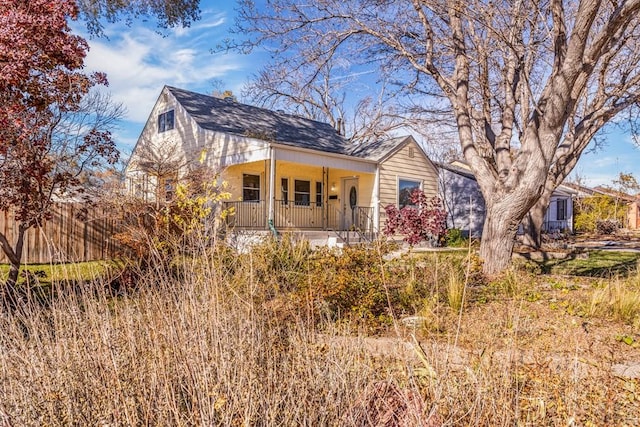 bungalow-style home featuring covered porch, roof with shingles, and fence