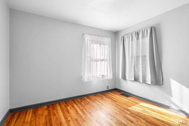 empty room with wood finished floors, visible vents, and baseboards