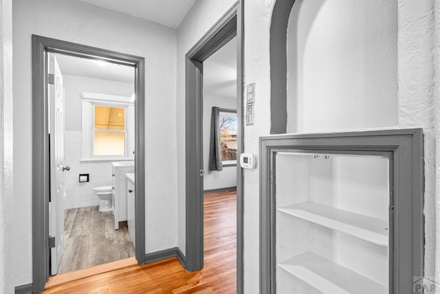 hall featuring a textured wall, wood finished floors, and tile walls