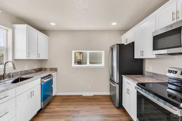 kitchen featuring light wood-style flooring, light stone counters, appliances with stainless steel finishes, white cabinetry, and a sink