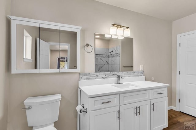 bathroom featuring tiled shower, toilet, wood finished floors, vanity, and backsplash