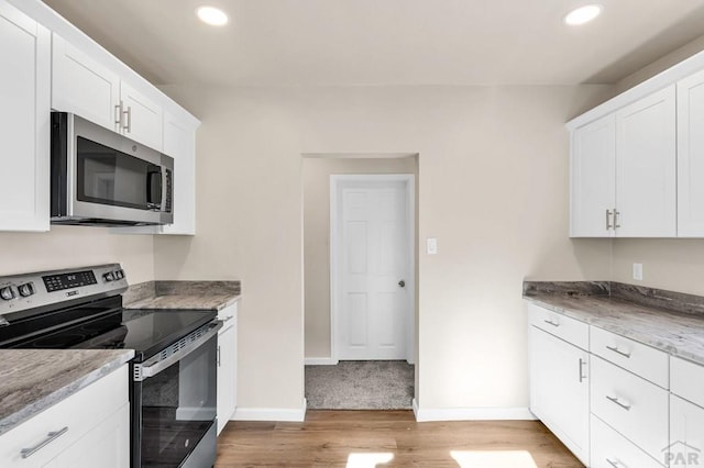 kitchen with appliances with stainless steel finishes, white cabinets, light wood-style floors, and light stone counters