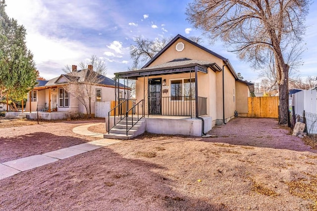 view of front of home with covered porch, fence, and stucco siding