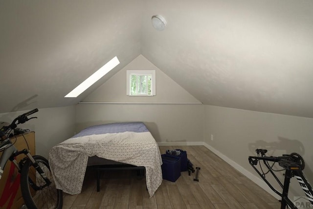 bedroom with lofted ceiling with skylight, wood finished floors, and baseboards