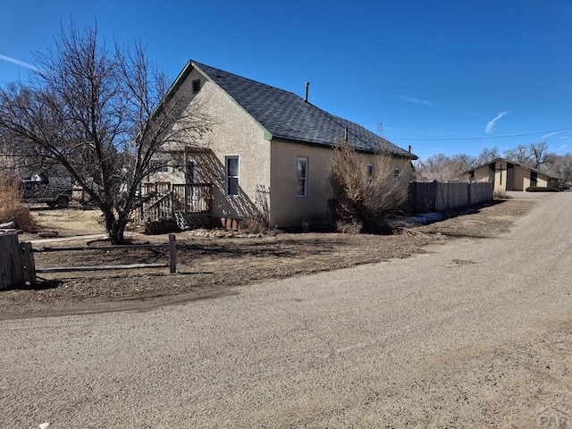 view of home's exterior with roof with shingles, fence, and stucco siding