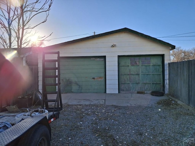 garage at dusk featuring fence and a detached garage