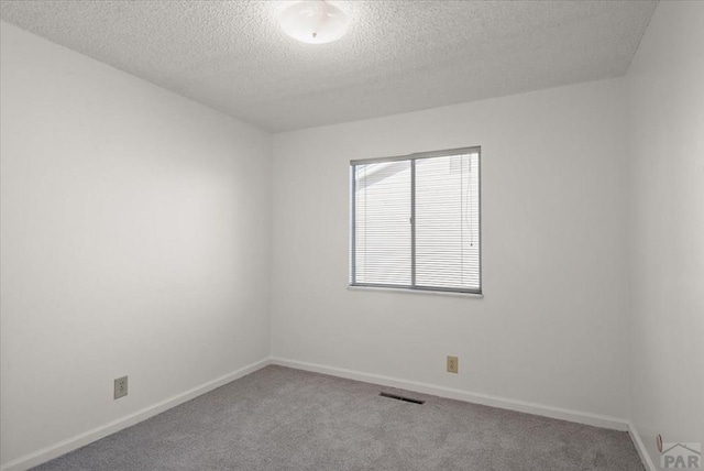 spare room with light carpet, visible vents, baseboards, and a textured ceiling