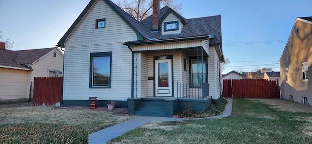 view of front facade featuring a shingled roof, fence, and a front lawn