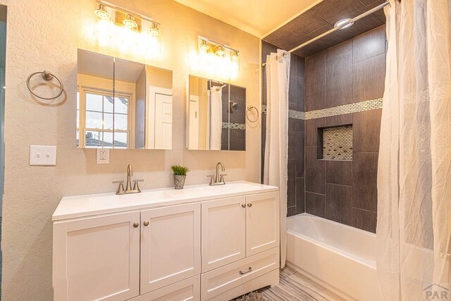 full bathroom featuring a textured wall, a sink, shower / bathtub combination with curtain, and double vanity