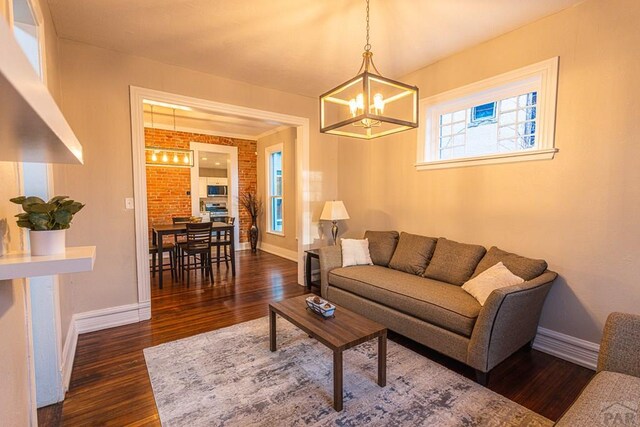 living area featuring brick wall, a notable chandelier, dark wood finished floors, and baseboards