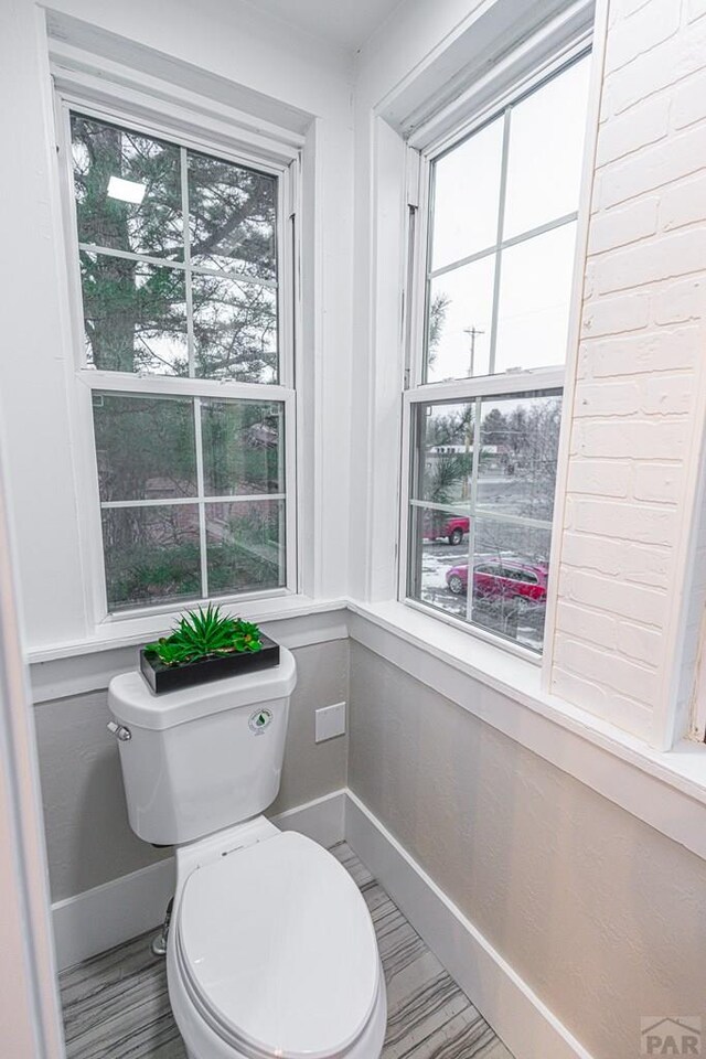 bathroom featuring baseboards, toilet, and a healthy amount of sunlight