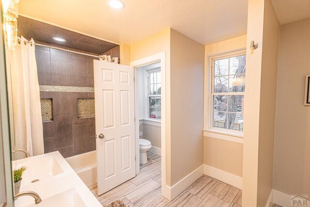 bathroom featuring baseboards, toilet, shower / tub combo with curtain, dual sinks, and recessed lighting