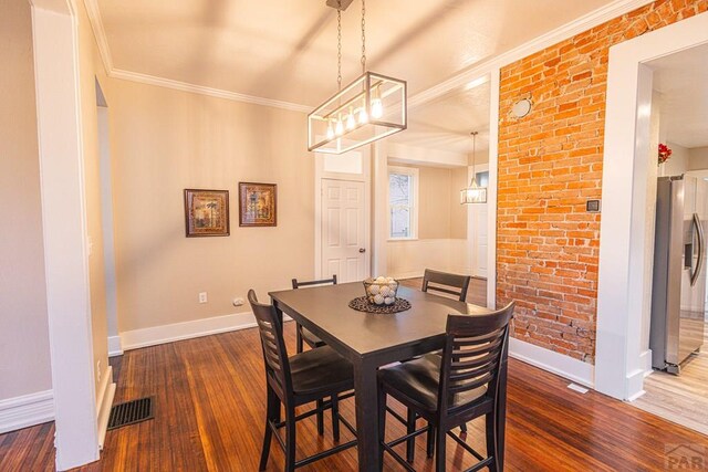 dining space featuring dark wood-style floors, brick wall, ornamental molding, and baseboards