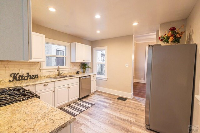 kitchen with white cabinets, light stone countertops, stainless steel appliances, and a sink