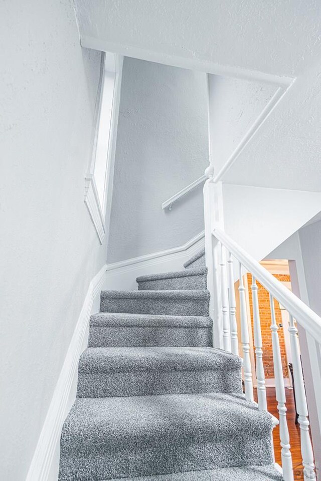 staircase with a textured ceiling, baseboards, and wood finished floors