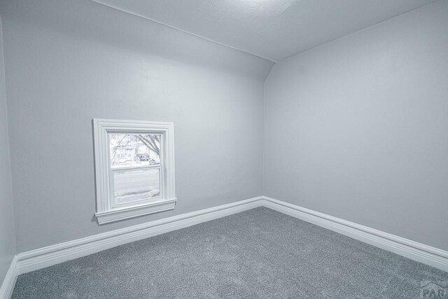 carpeted empty room featuring baseboards and vaulted ceiling