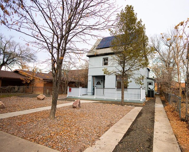 view of front facade with central AC, stucco siding, fence private yard, and roof mounted solar panels