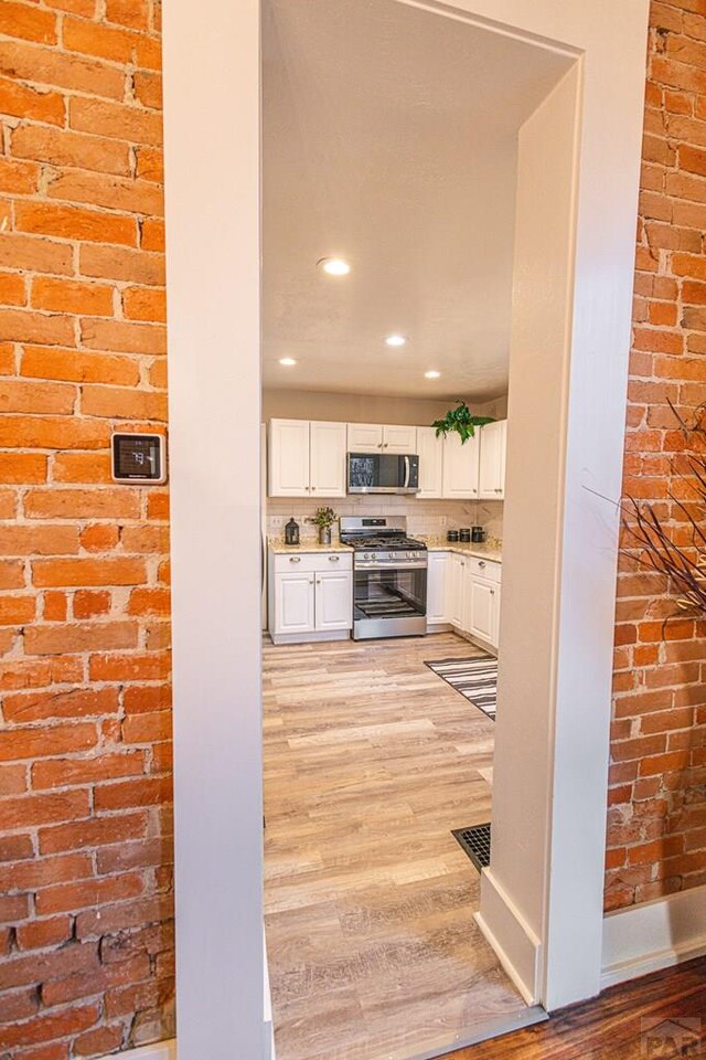 kitchen featuring brick wall, white cabinetry, light countertops, appliances with stainless steel finishes, and light wood-type flooring