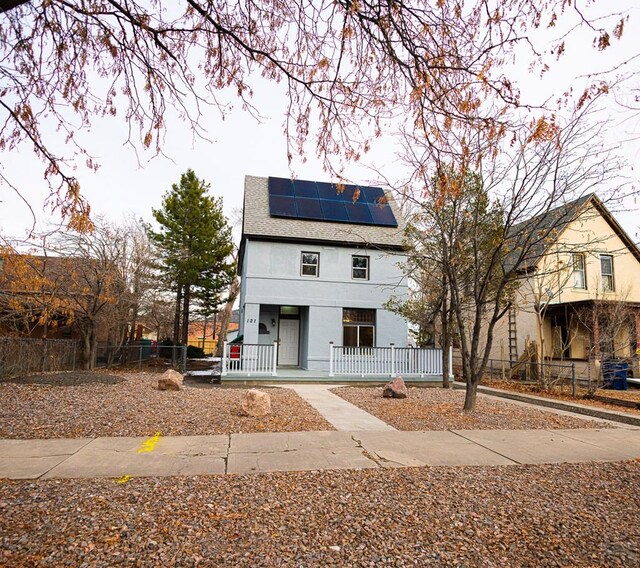 view of front of property featuring a fenced front yard, roof mounted solar panels, roof with shingles, and stucco siding