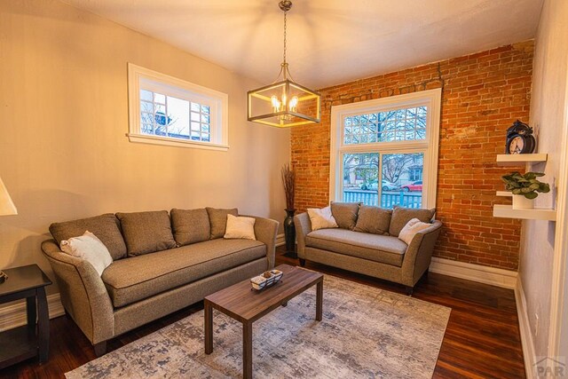 living area featuring dark wood-type flooring, baseboards, brick wall, and an inviting chandelier