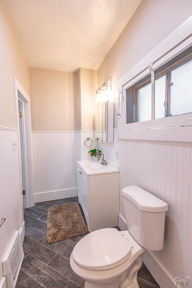 bathroom with wood finish floors, a wainscoted wall, visible vents, toilet, and vanity