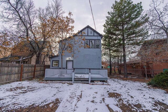 snow covered house featuring fence and a wooden deck