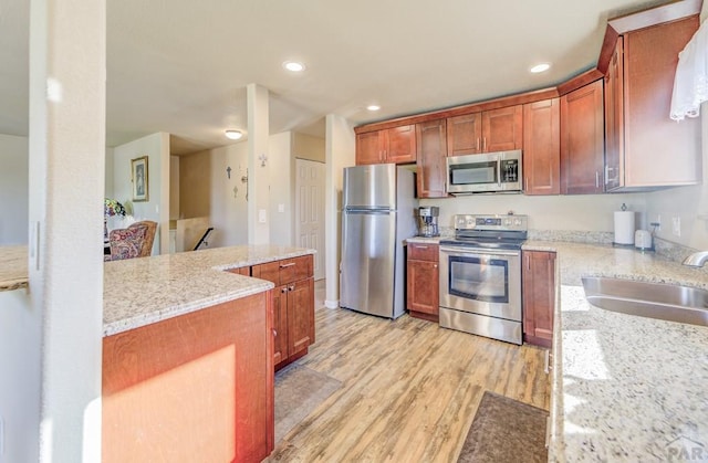 kitchen featuring light stone countertops, recessed lighting, light wood-style flooring, appliances with stainless steel finishes, and a sink