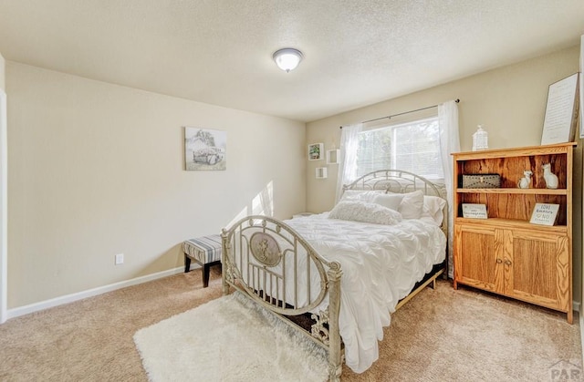 bedroom featuring light carpet, a textured ceiling, and baseboards