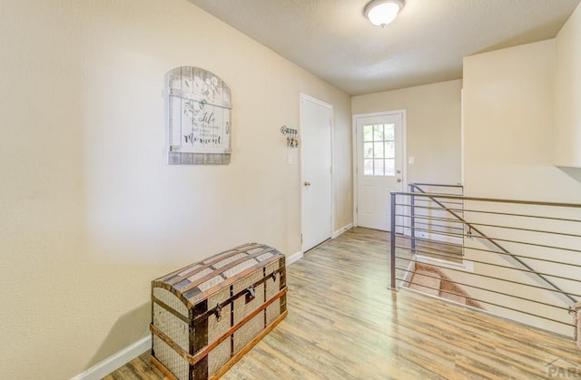 hallway with an upstairs landing, a textured ceiling, baseboards, and wood finished floors