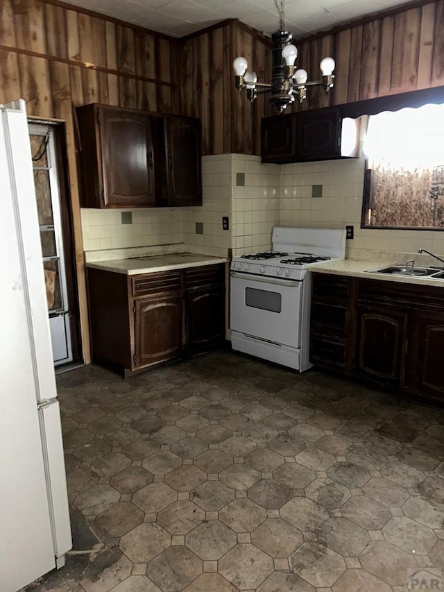 kitchen with light countertops, a sink, dark brown cabinets, a chandelier, and white appliances