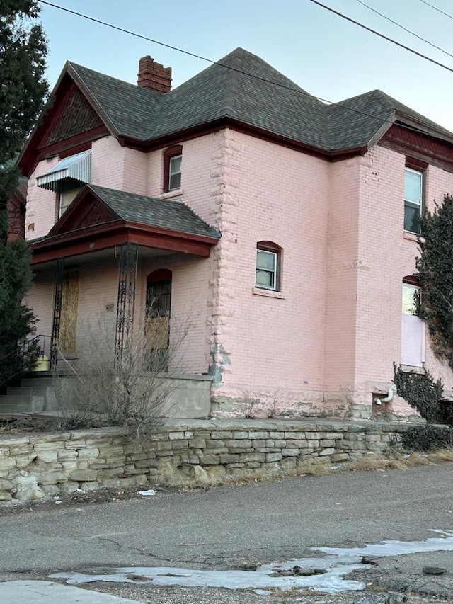 view of property exterior with brick siding, a chimney, and roof with shingles