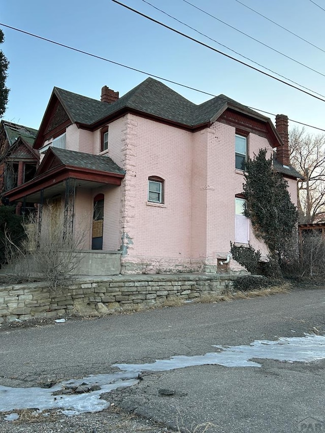 view of property exterior with a shingled roof, brick siding, and a chimney