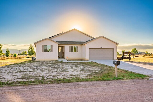 ranch-style home featuring a garage, concrete driveway, central AC unit, and stucco siding