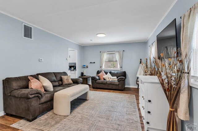 living area with ornamental molding, visible vents, baseboards, and wood finished floors