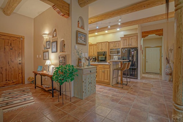 kitchen with light countertops, light brown cabinetry, black appliances, beamed ceiling, and a kitchen bar