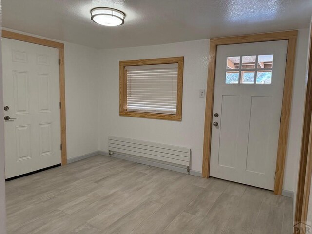 foyer entrance featuring radiator heating unit, baseboards, a textured ceiling, and light wood finished floors