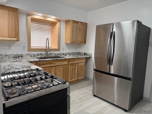 kitchen with baseboards, light stone counters, freestanding refrigerator, a sink, and gas stove