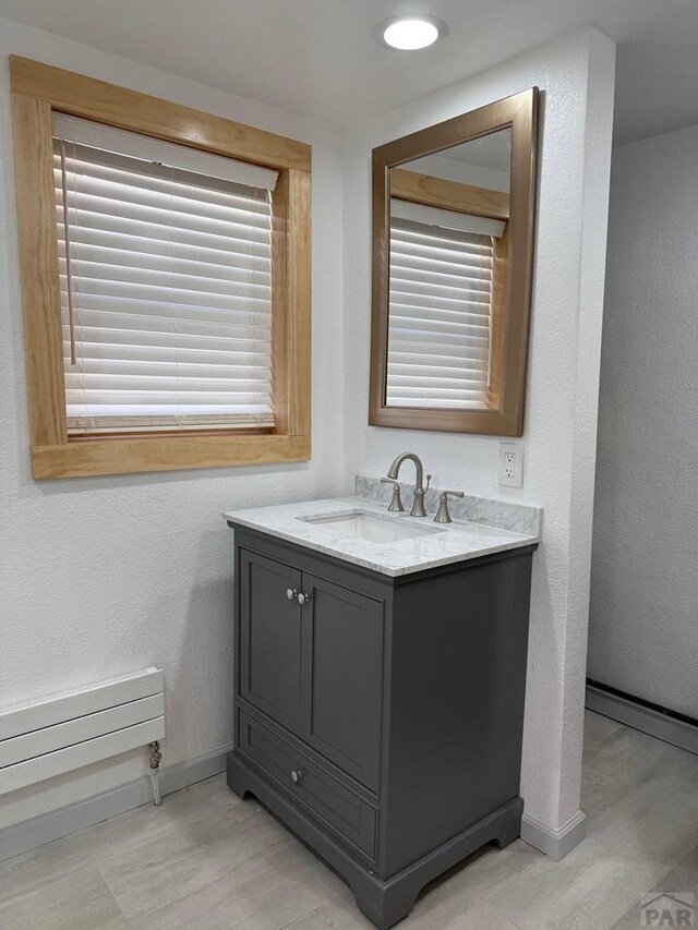 bathroom with a textured wall, baseboards, wood finished floors, and vanity